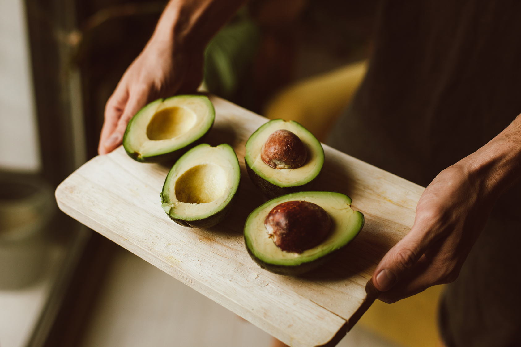 Close-Up Shot of a Person Holding a Wooden Tray with Sliced Avocados